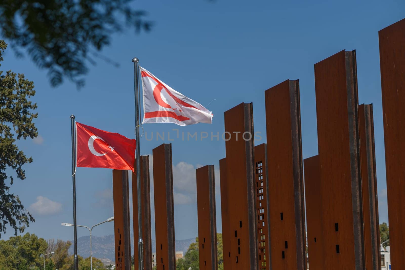 Flags of Turkey and Northern Cyprus flutter in the breeze, showcasing national pride near a contemporary monument. The bright blue sky adds a tranquil backdrop to this evocative setting.