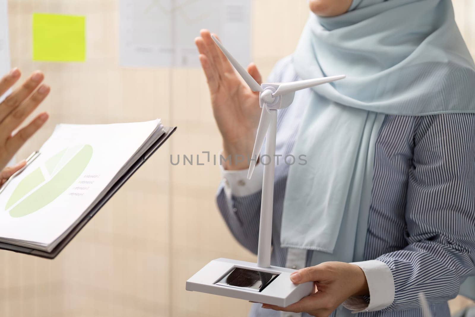 A woman explains the importance of wind energy using a model during a meeting, illustrating the impact of sustainable practices on business decisions.