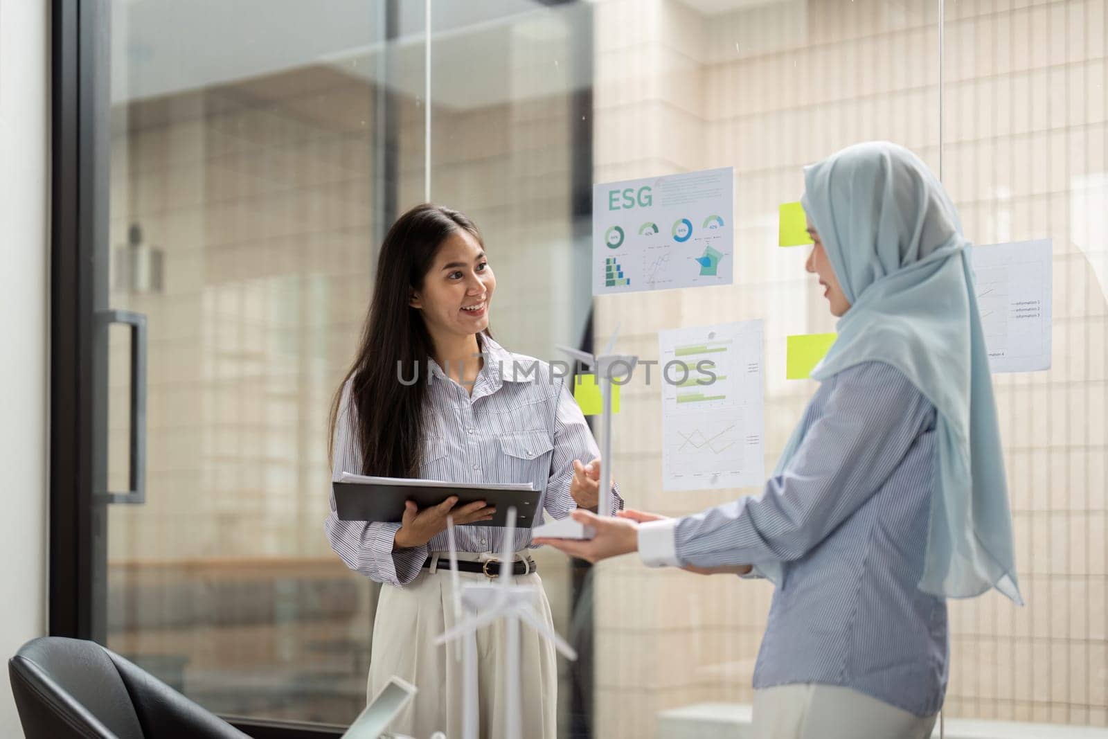 Two women communicate at their workplace about ESG strategies and sustainability measures, highlighting how renewable energy contributes to corporate responsibility and social impact.