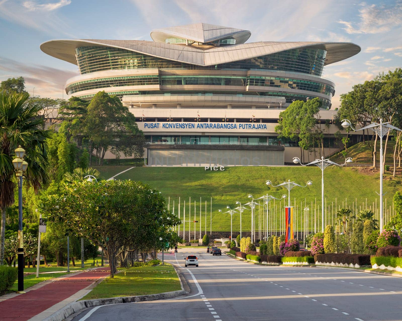 The Pusat Konvensyen Antarabangsa in Putrajaya, Malaysia, stands prominently amidst lush greenery and designed pathways, highlighting its striking architecture and inviting environment