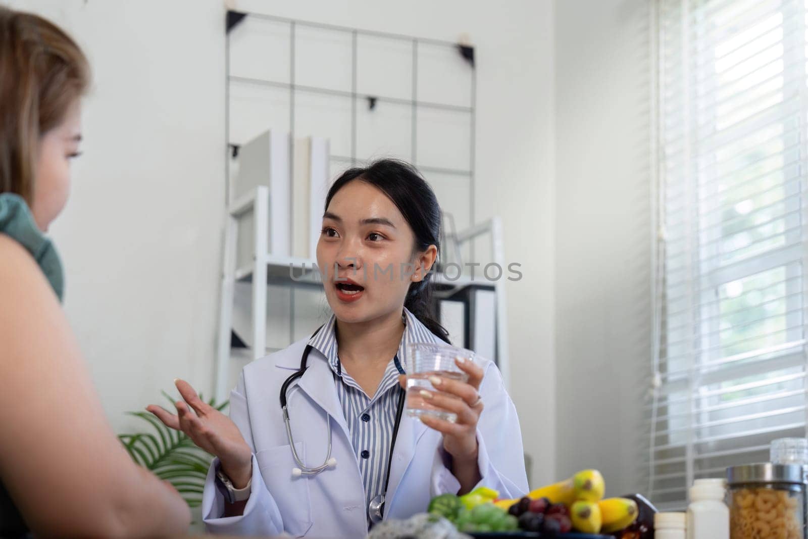 A healthcare provider explains the importance of hydration and nutrition during a consultation while showcasing various healthy foods.