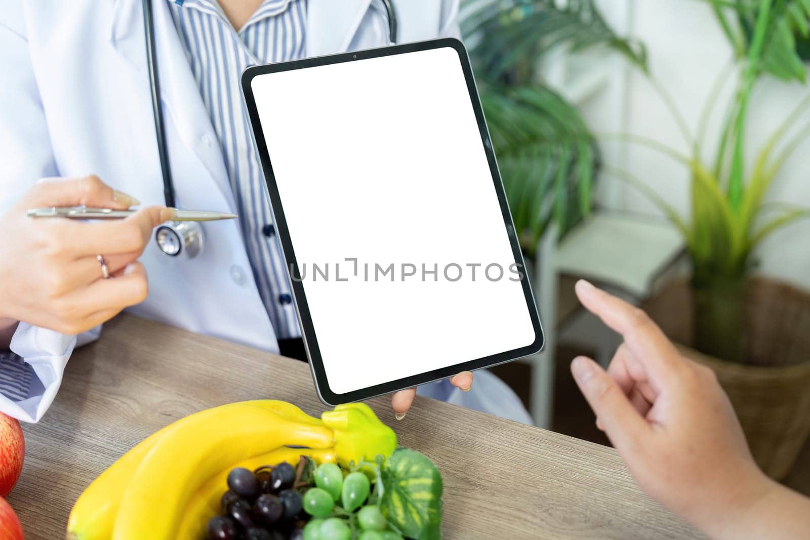 A nutritionist demonstrates meal planning on a tablet, visually engaging the patient to discuss healthy food choices alongside colorful fruits.