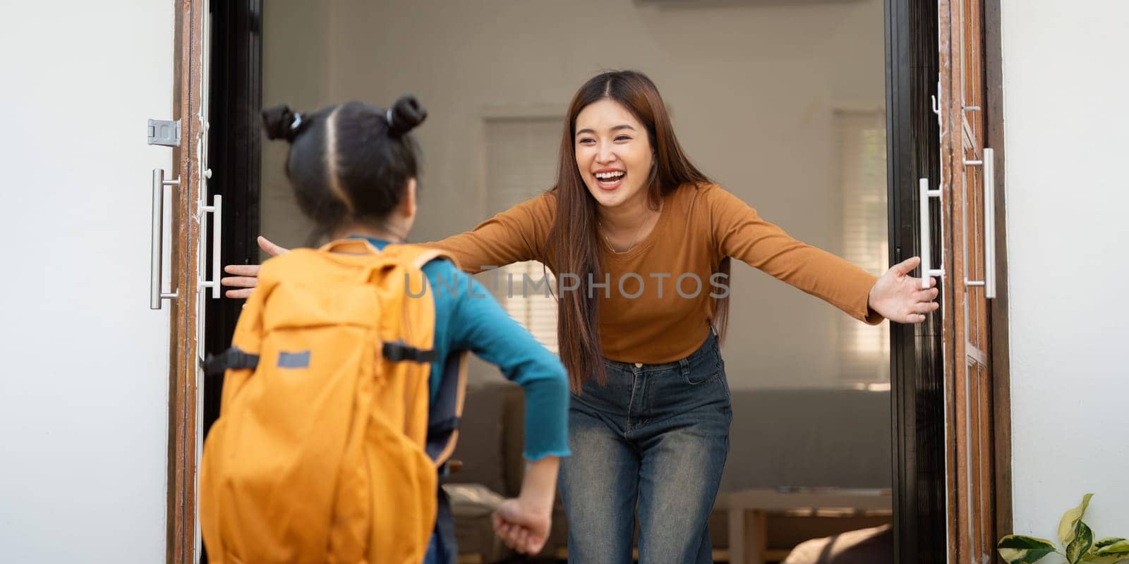 A delightful scene as a young girl enters her home, running into the arms of her parent, filled with warmth and excitement after a day at school.
