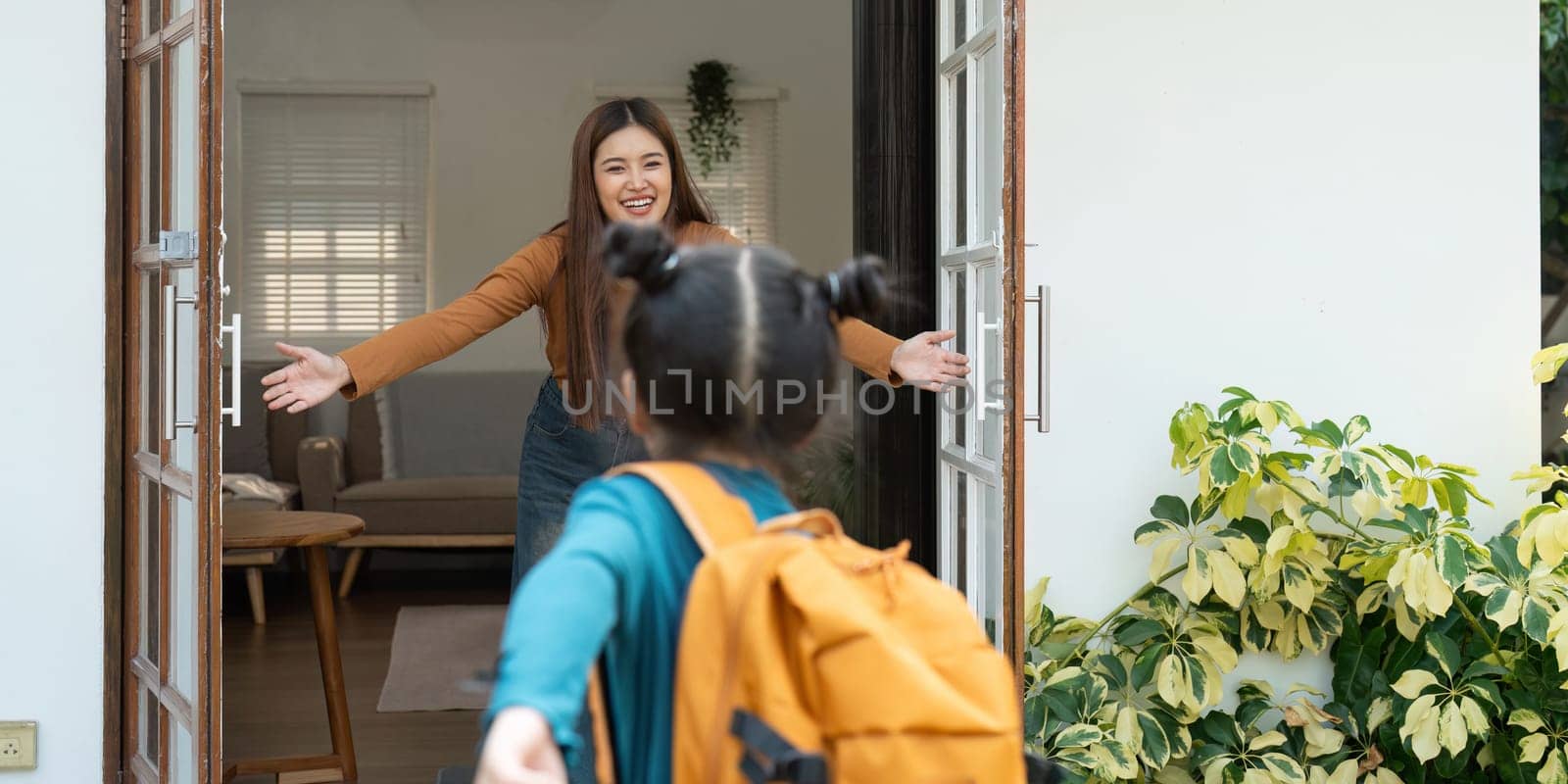 After a day at school, a girl joyfully rushes to her mother, who greets her with open arms. This moment captures the excitement and love shared between them.