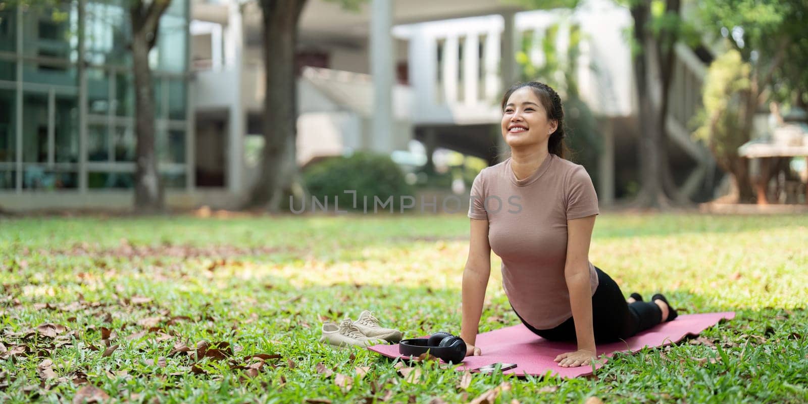 In a grassy area, a woman enjoys her yoga session, showcasing her dedication to wellness and personal growth through mindful movement.