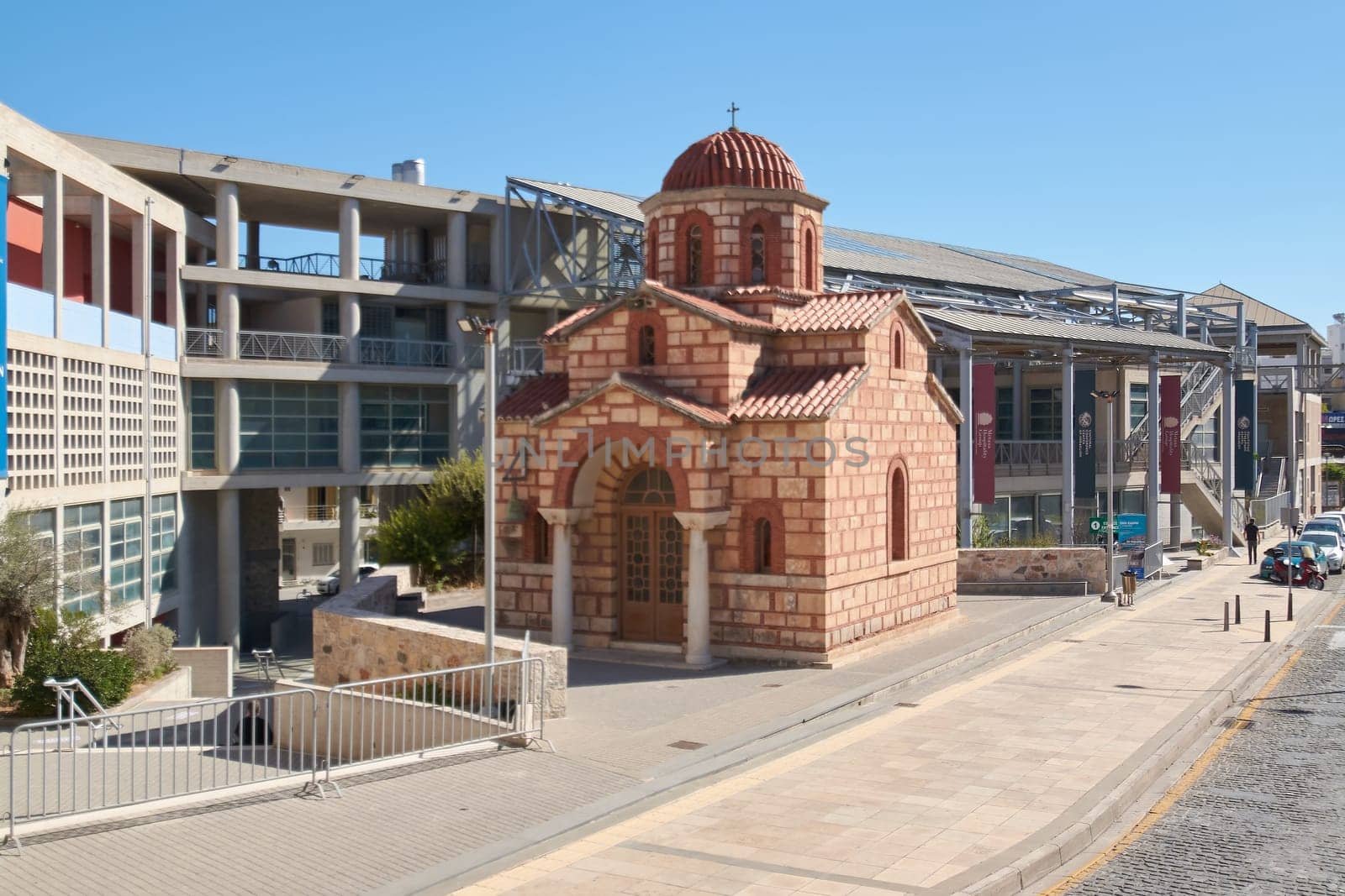 Crete.Greece - april 11, 2025: A small Byzantine-style church with intricate stonework and a red dome stands among modern city structures. The blend of ancient and contemporary elements creates a striking visual contrast