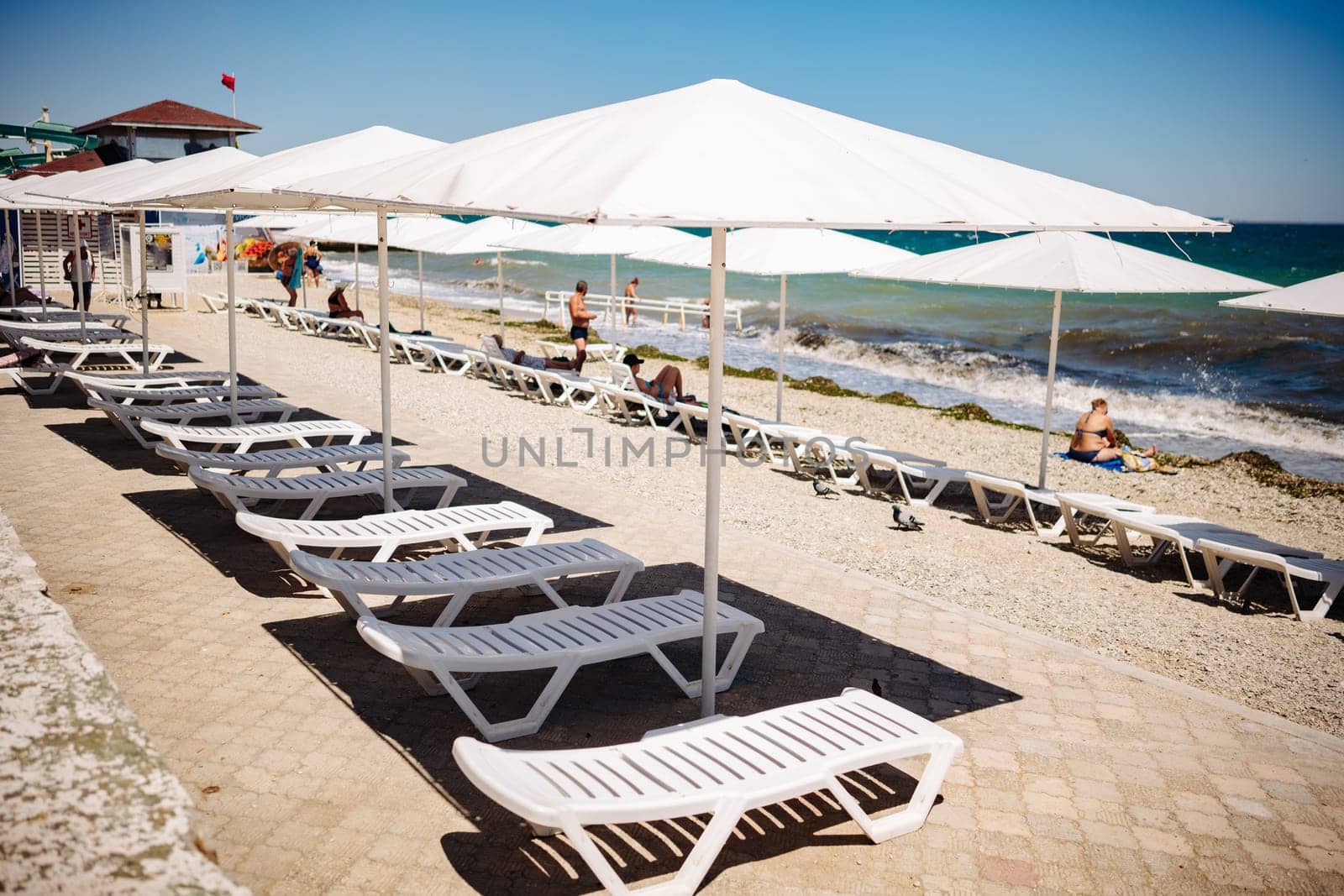 Tourists enjoying summer holidays on the beach of Koktebel, Crimea, relaxing on white sunbeds under white parasols