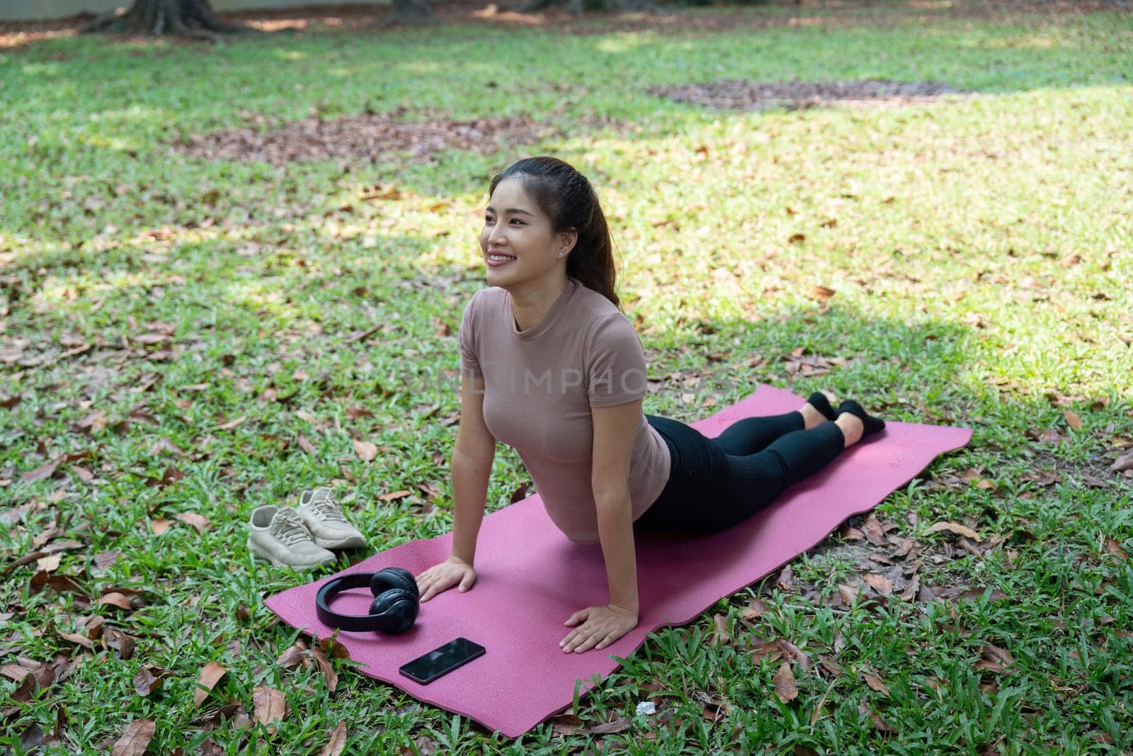 A smiling woman enjoys her yoga practice in an outdoor setting, embodying wellness and routine, reinforcing her physical and mental health.