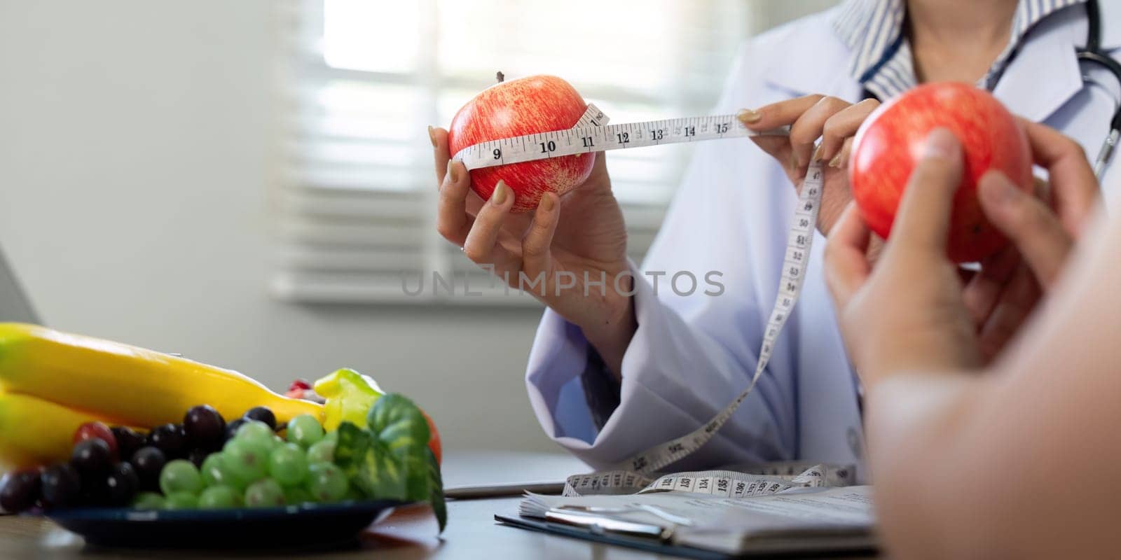 During a consultation, a nutritionist uses a measuring tape around apples to educate her patient on portion size and healthy eating practices.