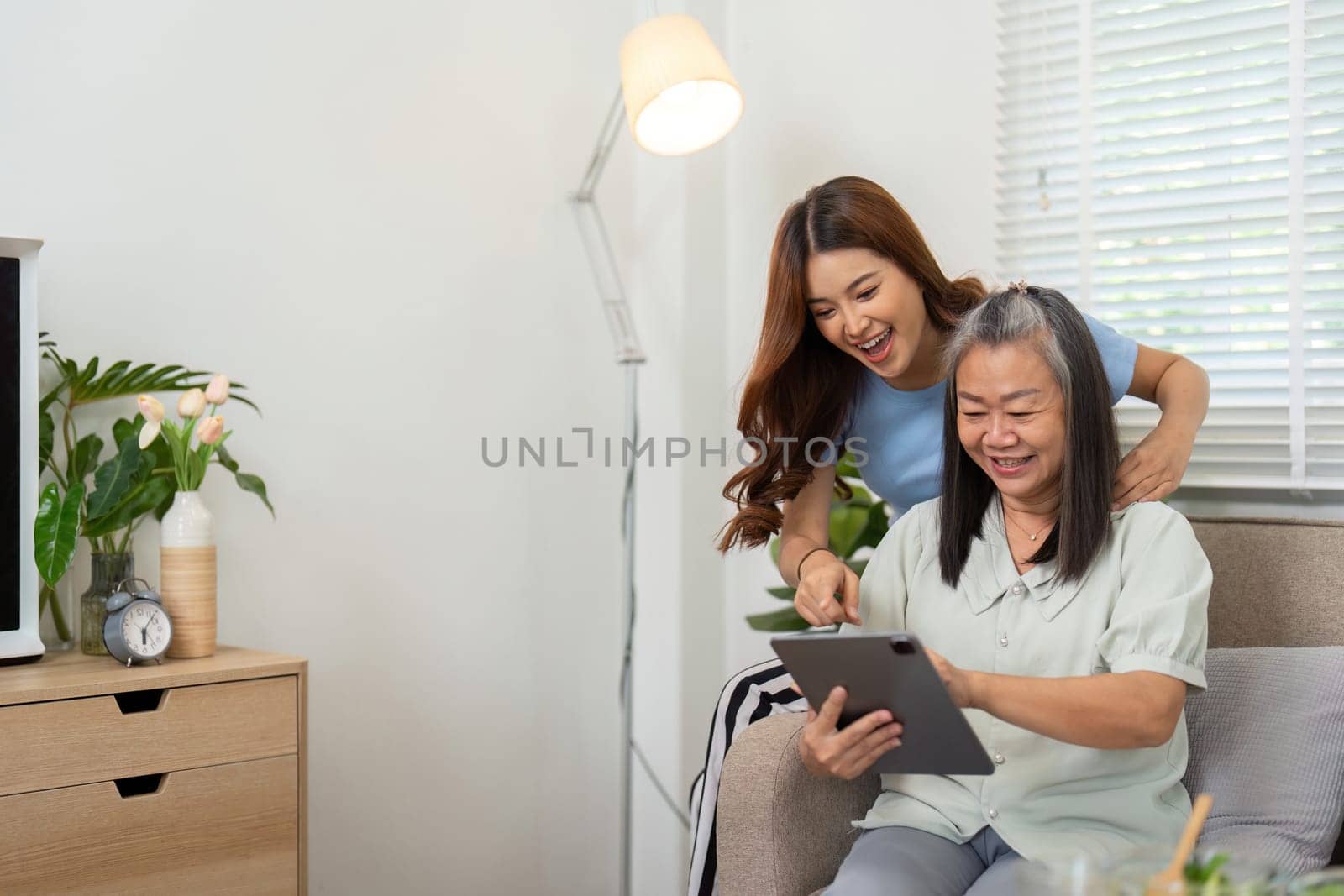 In a comfortable living room, a mother and daughter interact joyfully while exploring content together on a tablet, reinforcing their connection through technology.