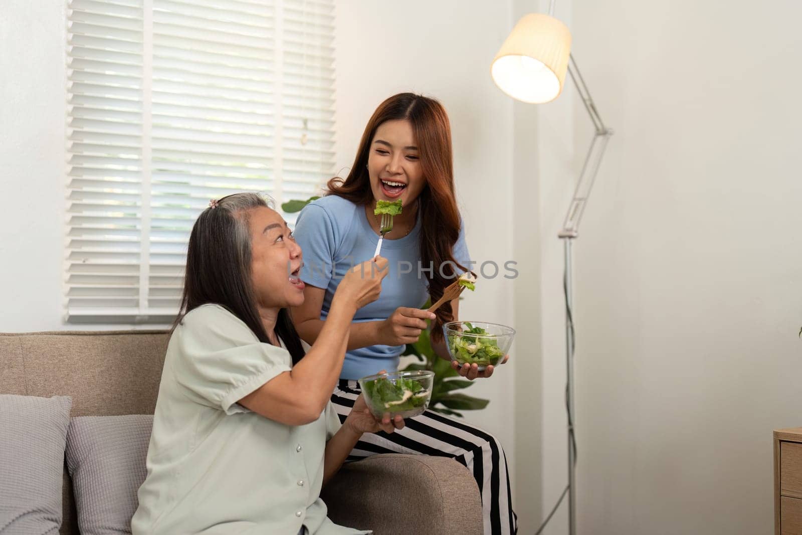 The mother and daughter share laughter while munching on a colorful salad, emphasizing the importance of wellness in their daily life.