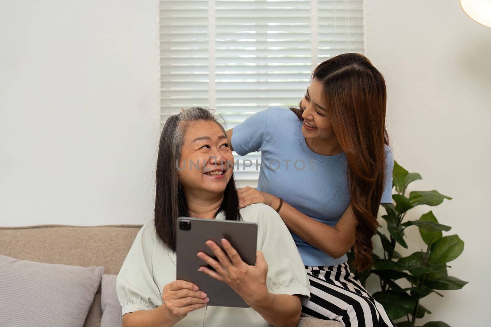 In a bright living room, the daughter surprises her mother with a fun digital activity, blending technology with healthy family bonding.