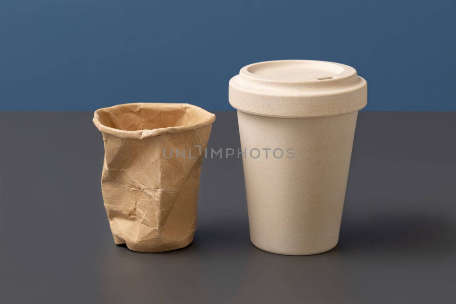 Used and crumpled disposable paper cup and reusable bamboo coffee cup on gray against blue closeup, copy space , mockup. Consumerism concept. No plastic and sustainable lifestyle concept