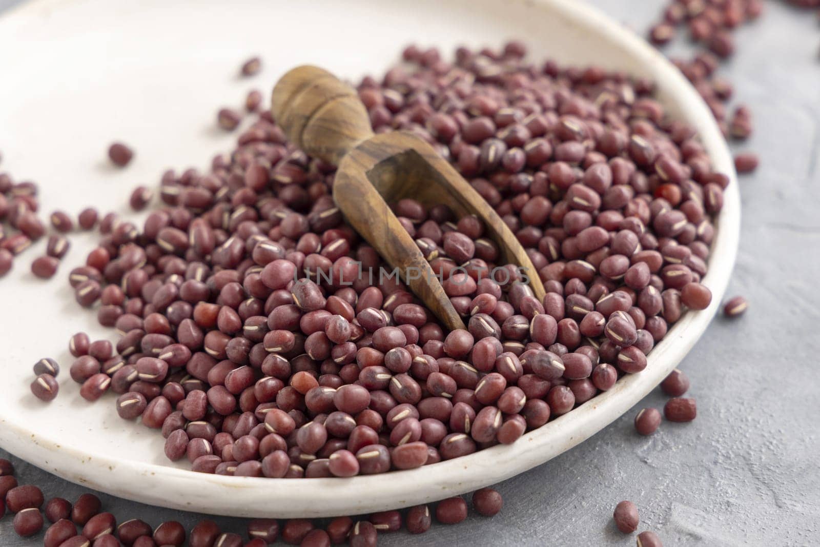 Ceramic plate full of dried red azuki beans with a wooden scoop closeup. Healthy vegetarian food, legumes protein source. Traditional East Asian cousin ingredient