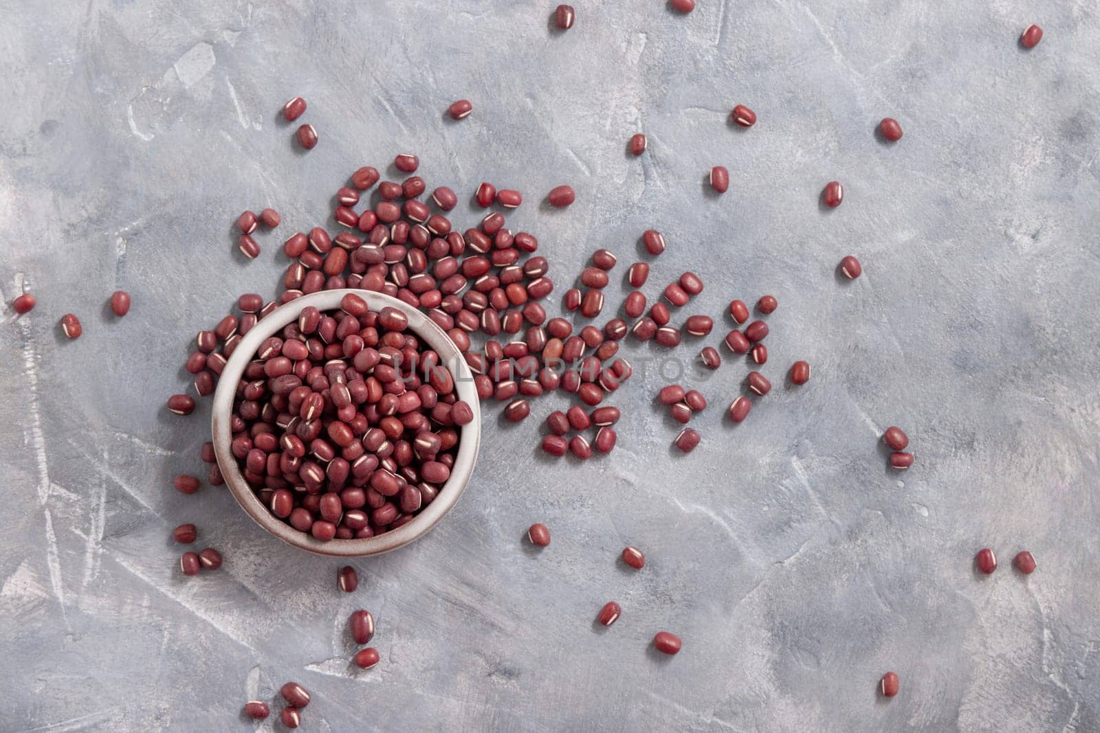 Ceramic bowl full of dried azuki beans on gray table top view. Healthy vegetarian food, legumes protein source. Traditional East Asiancousin ingredient