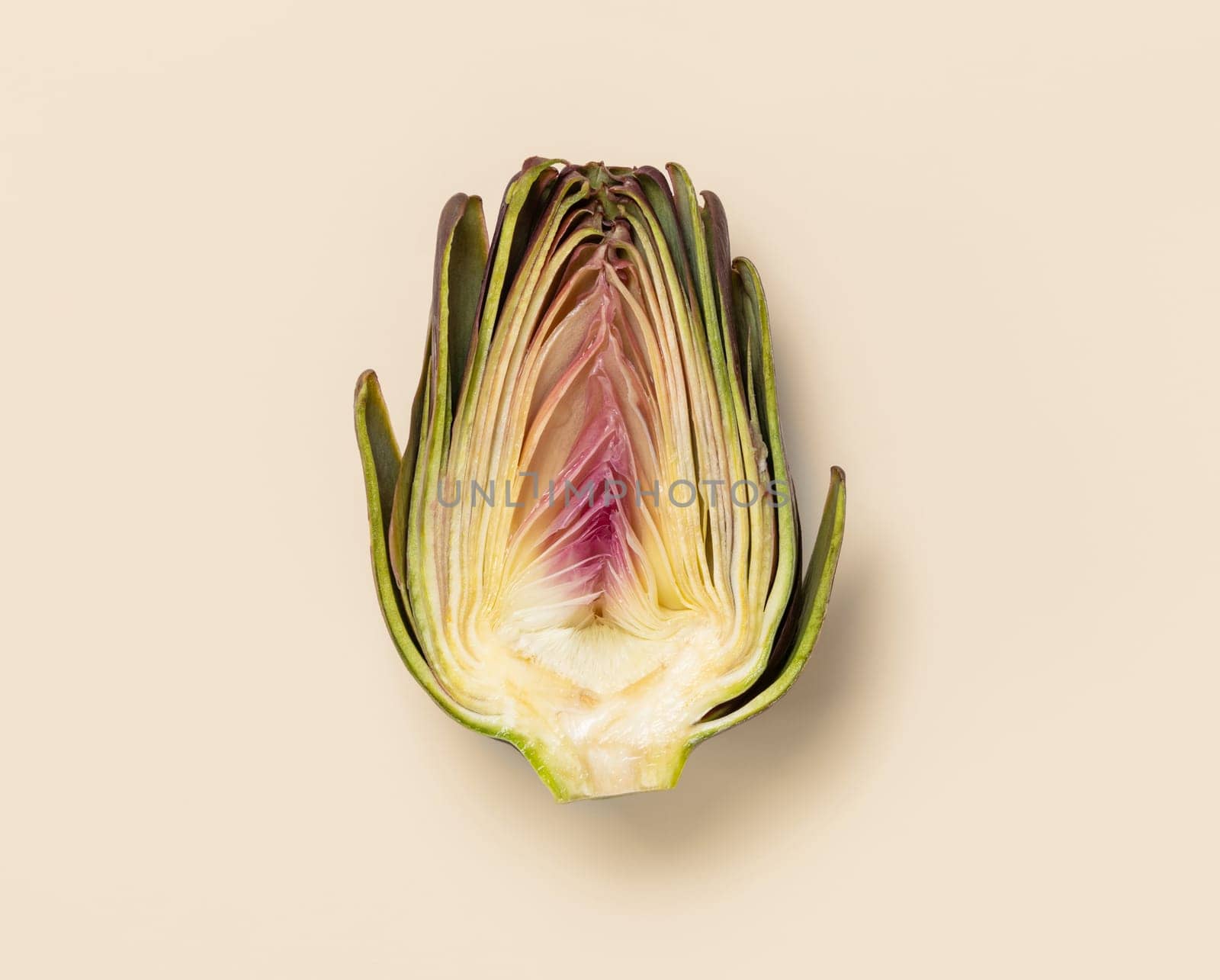 Cut raw purple artichoke on light yellow background top view. Fresh vegetables from farmers market ready to cook, vegetarian diet. Italian cousine ingredient