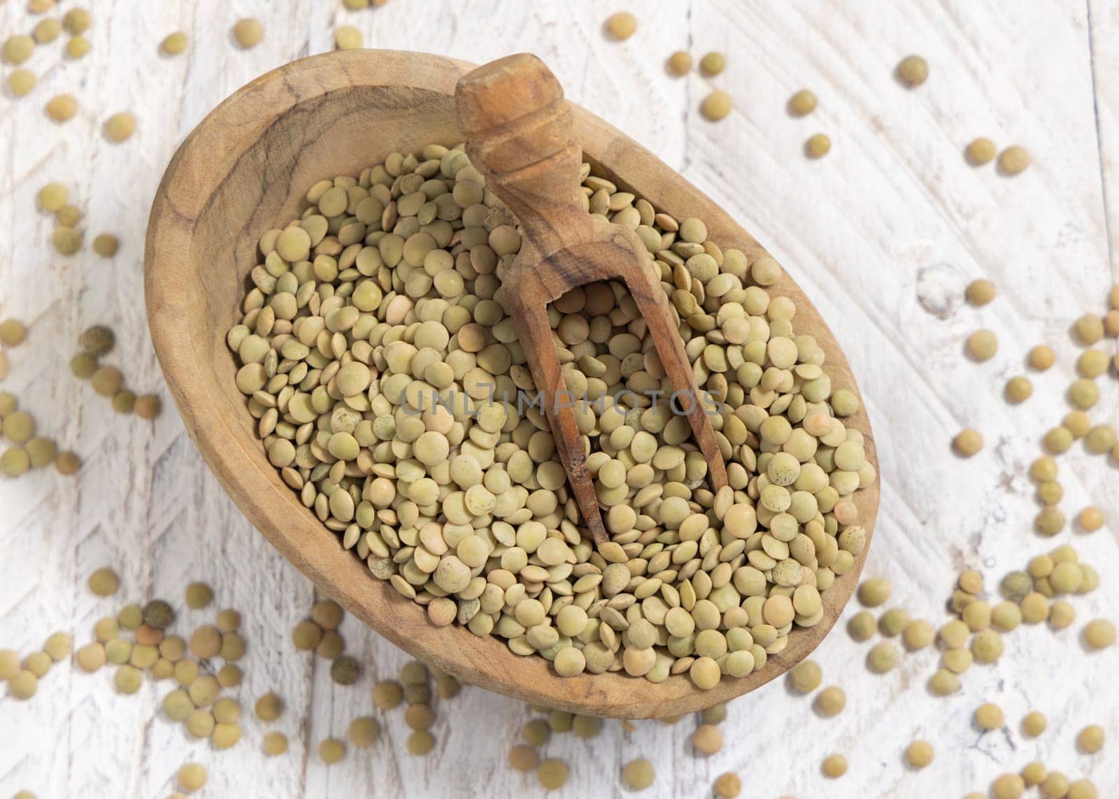Small bowl full of dried green lentils with a wooden scoop on white table top view. Healthy vegetarian food, legumes plant-based protein source. Traditional mediterranean raw uncooked ingredient