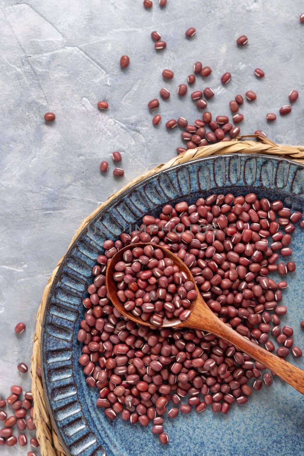Ceramic blue plate full of dried red azuki beans with a wooden spoon on grey table top view, copy space. Healthy vegetarian food, legumes protein source. Traditional East Asian cousin ingredient