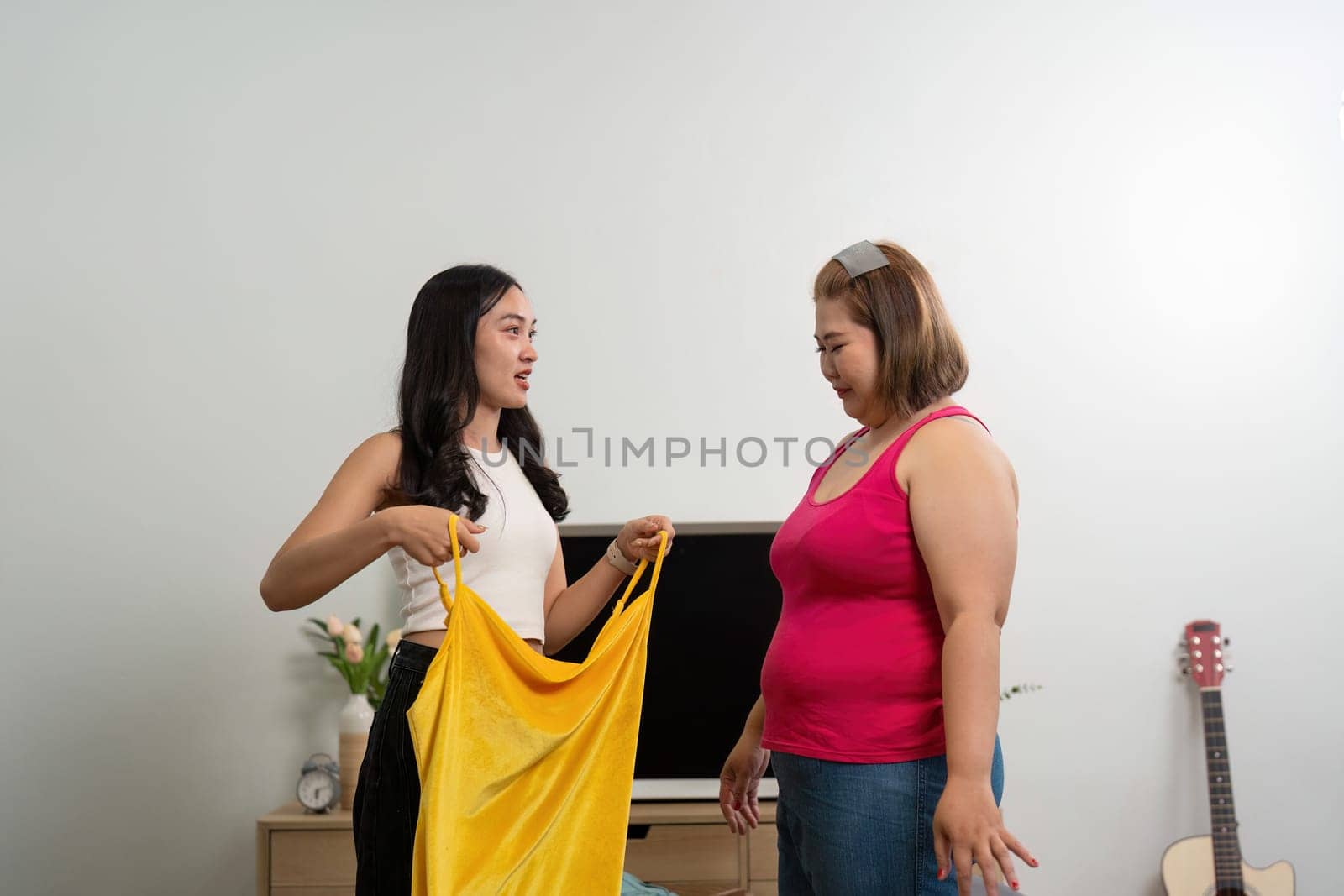 A stylist excitedly shows a bright yellow outfit to a client in a stylish living room, emphasizing personalized fashion choices and self-expression.