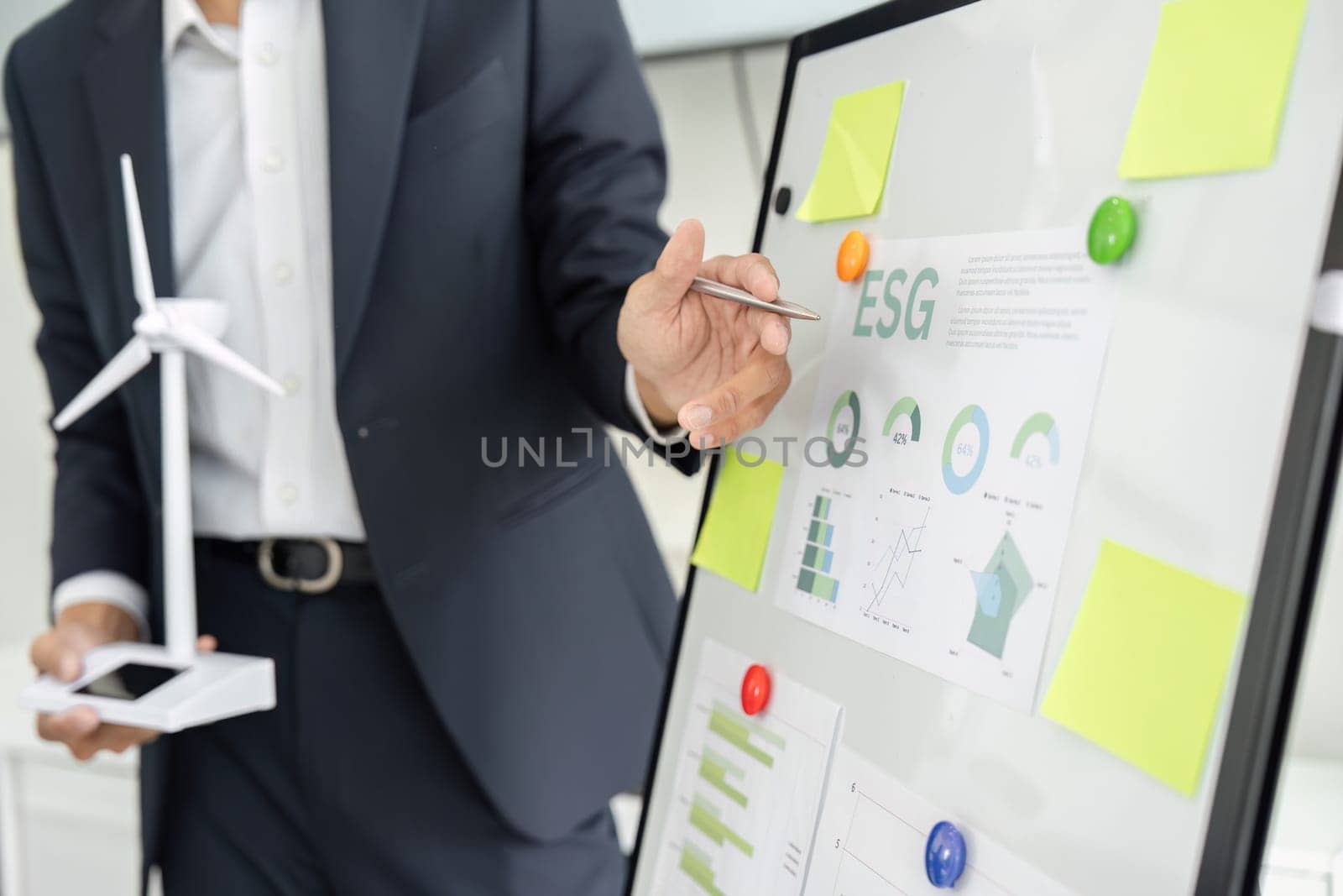 A business professional emphasizes key ESG statistics while holding a miniature wind turbine model, representing commitment to sustainability during the meeting.