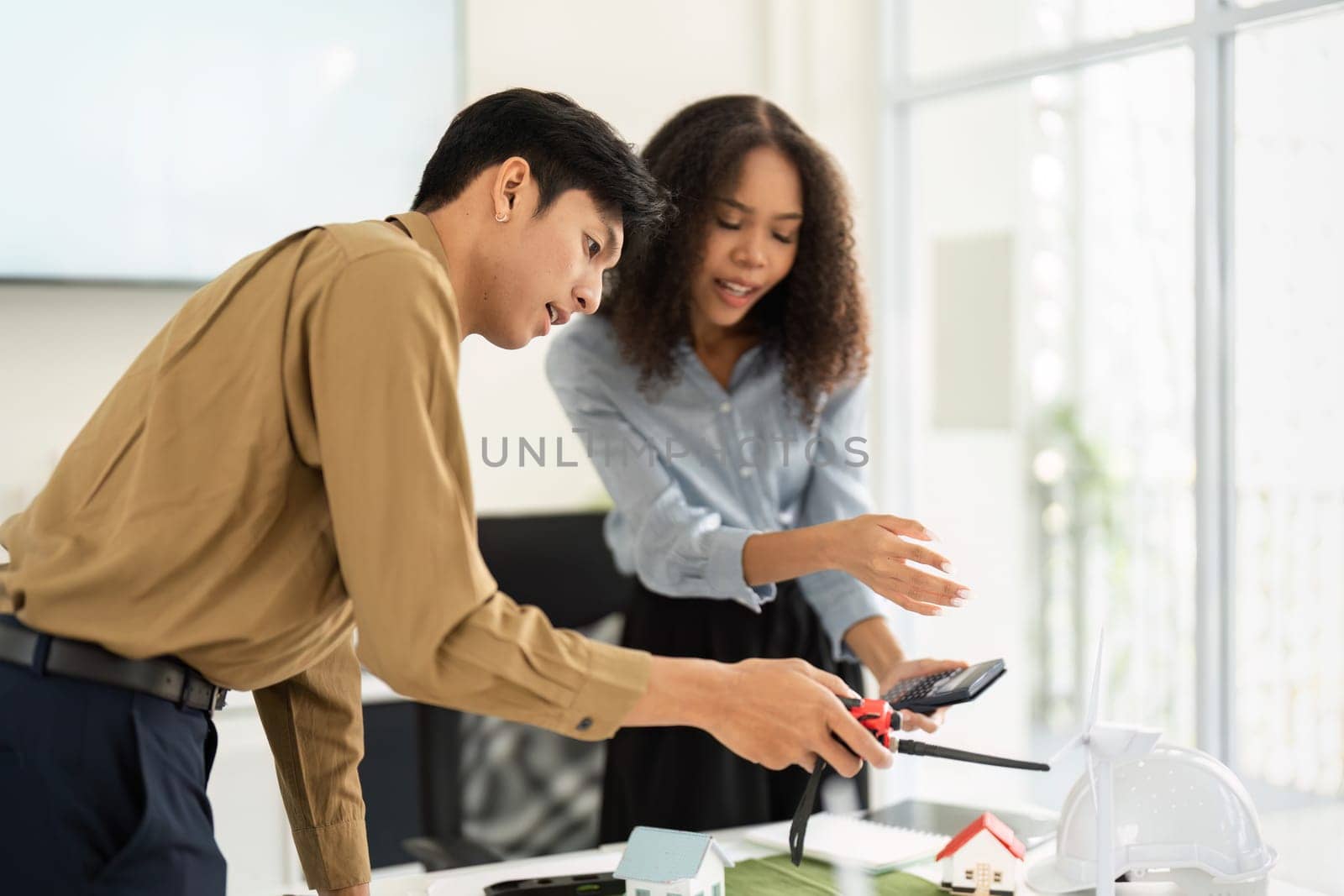 The duo actively collaborates on sustainable building practices, with models and materials spread across the table as they brainstorm ideas together.