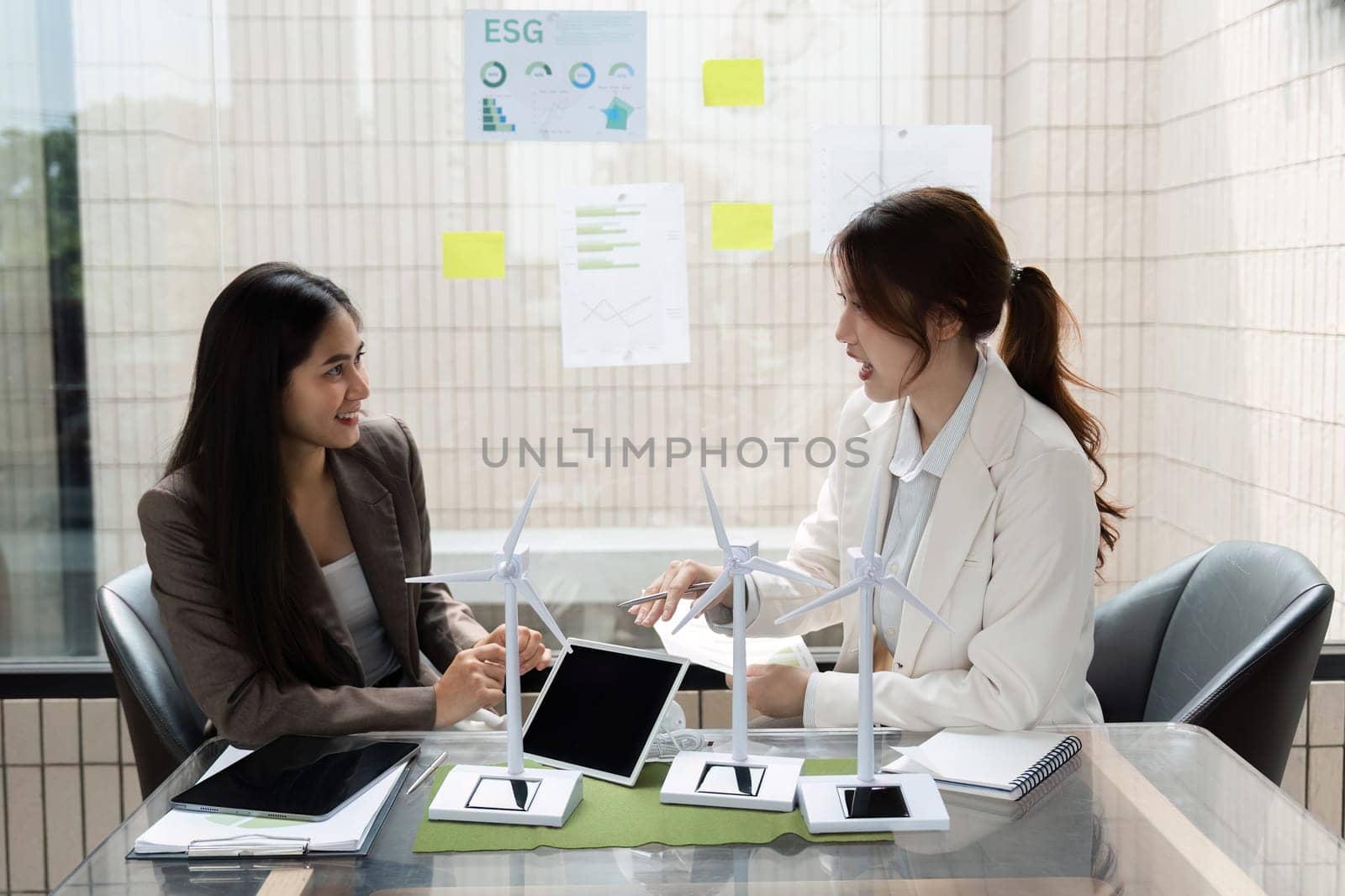 Two women share ideas and insights regarding ESG strategies, examining models of wind energy to enhance sustainability efforts in their company.
