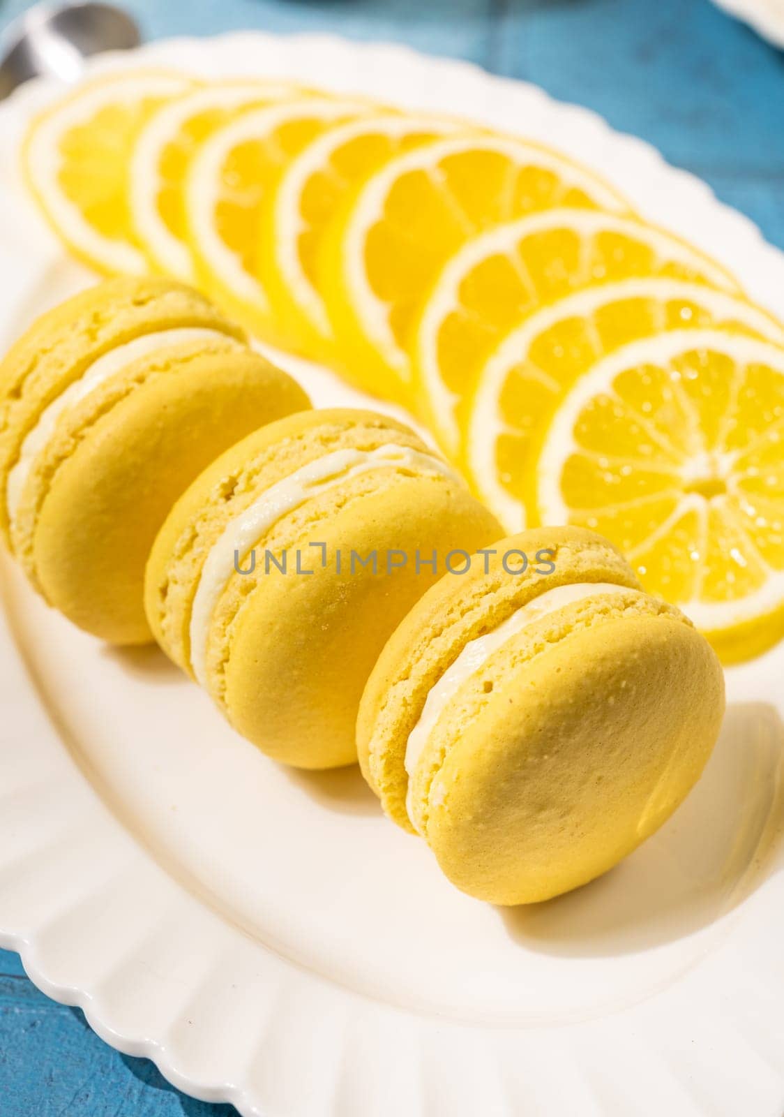Vibrant yellow lemon macarons arranged on a white plate, accompanied by freshly sliced lemons, creating a visually appealing dessert presentation