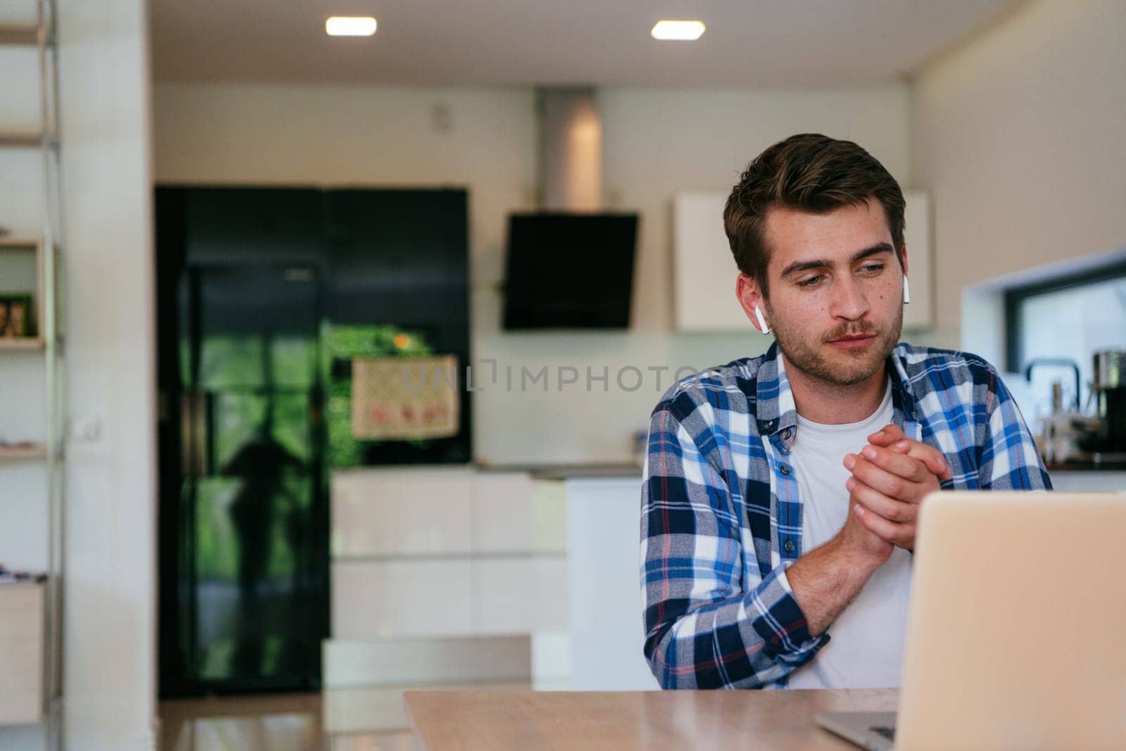A freelancer sitting at a table in a modern living room, with headphones using a laptop for business video chat, conversation with friends and entertainment.