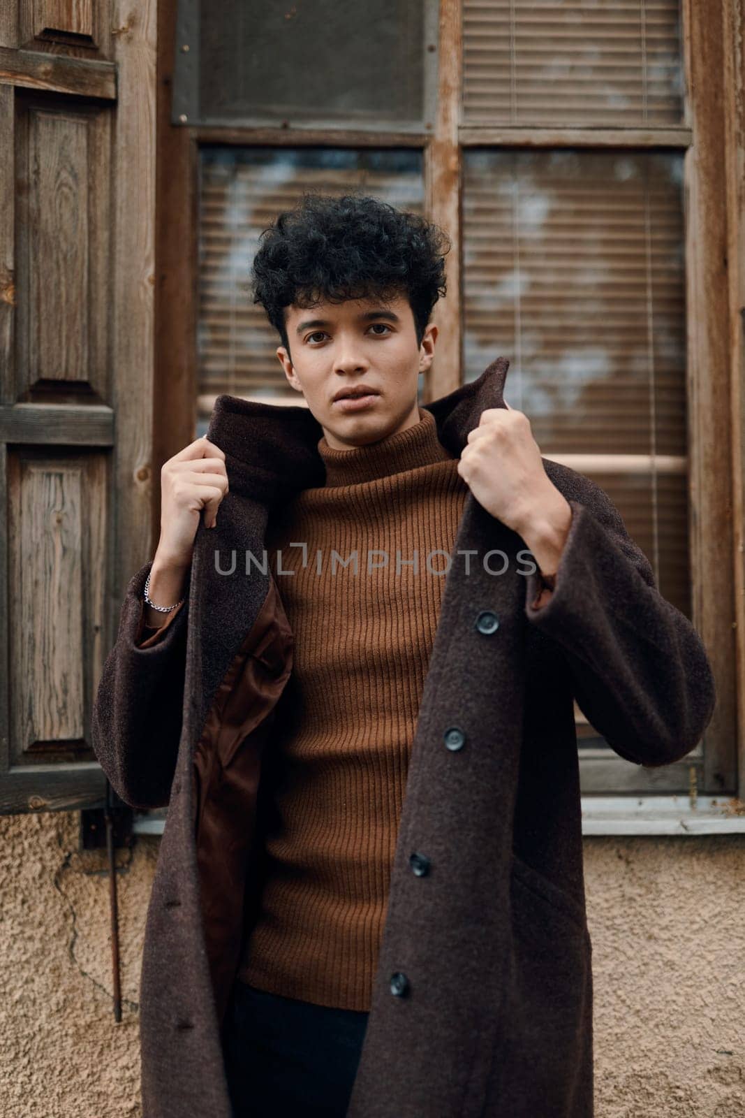 Fashion concept. young man in brown coat and turtleneck sweater standing in front of old building with open window.
