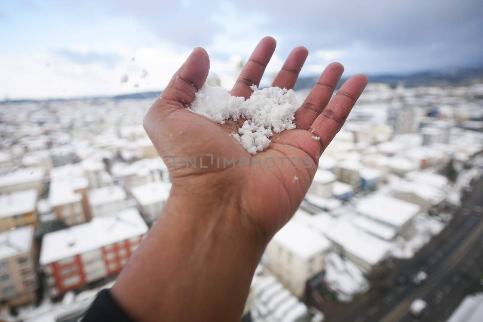 A hand offers fresh snow against a snowy urban background.