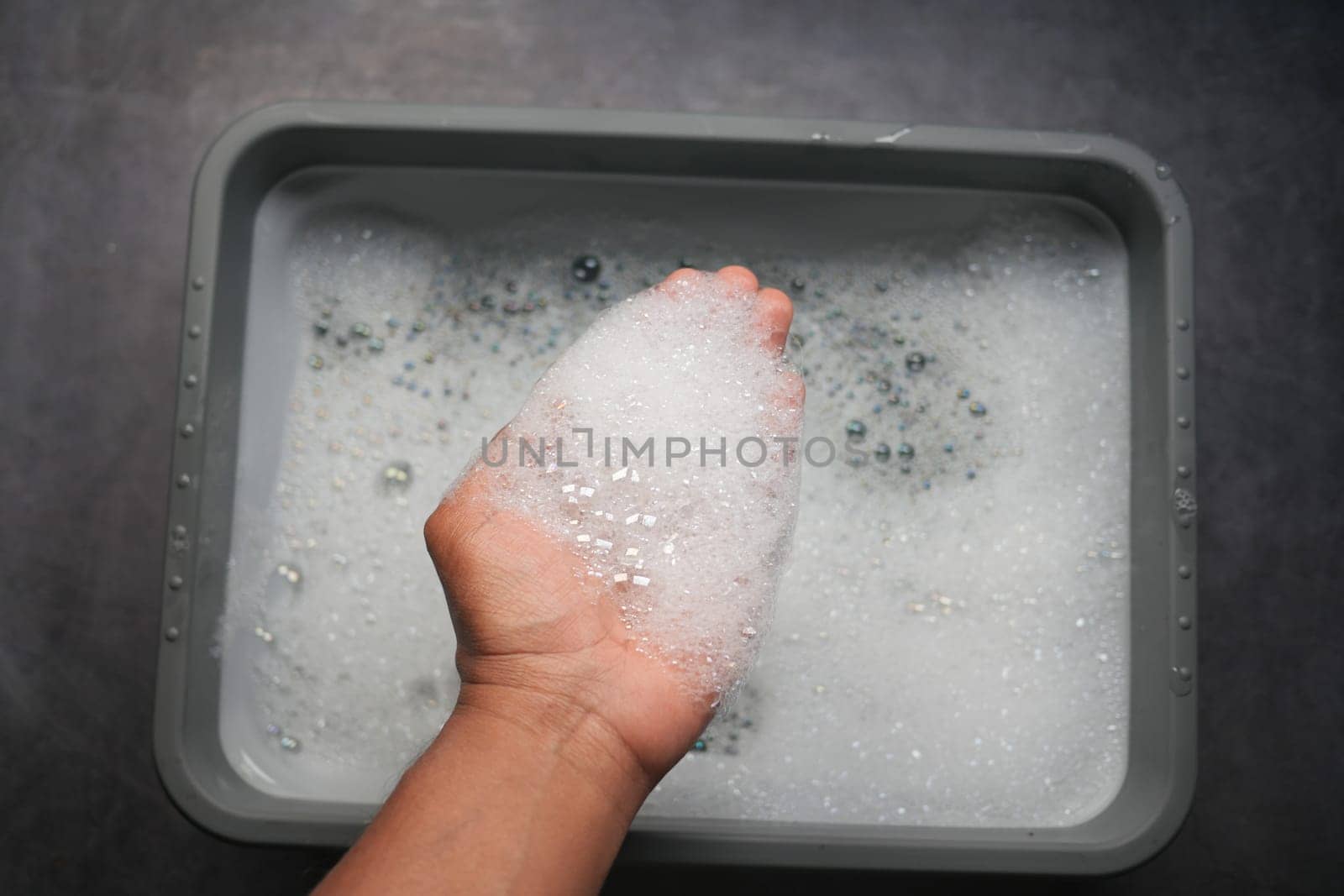 A hand holds a clump of bubbles above a basin of soapy water.