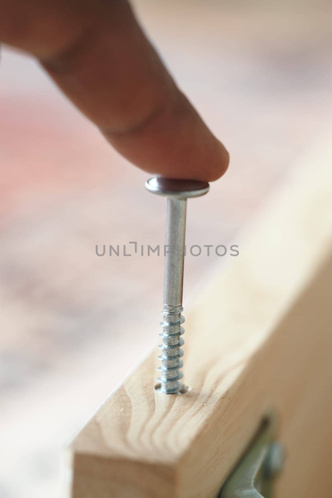 A finger hovers over a screw ready to be secured into timber.