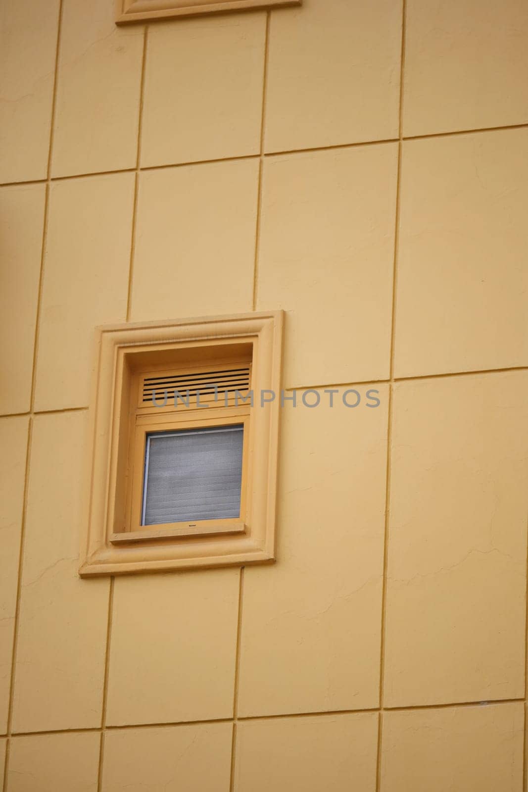 A small window is framed in wood against a vibrant yellow wall.
