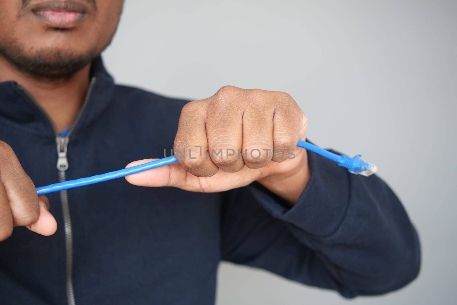 A man is intentionally breaking a blue Ethernet cable indoors.