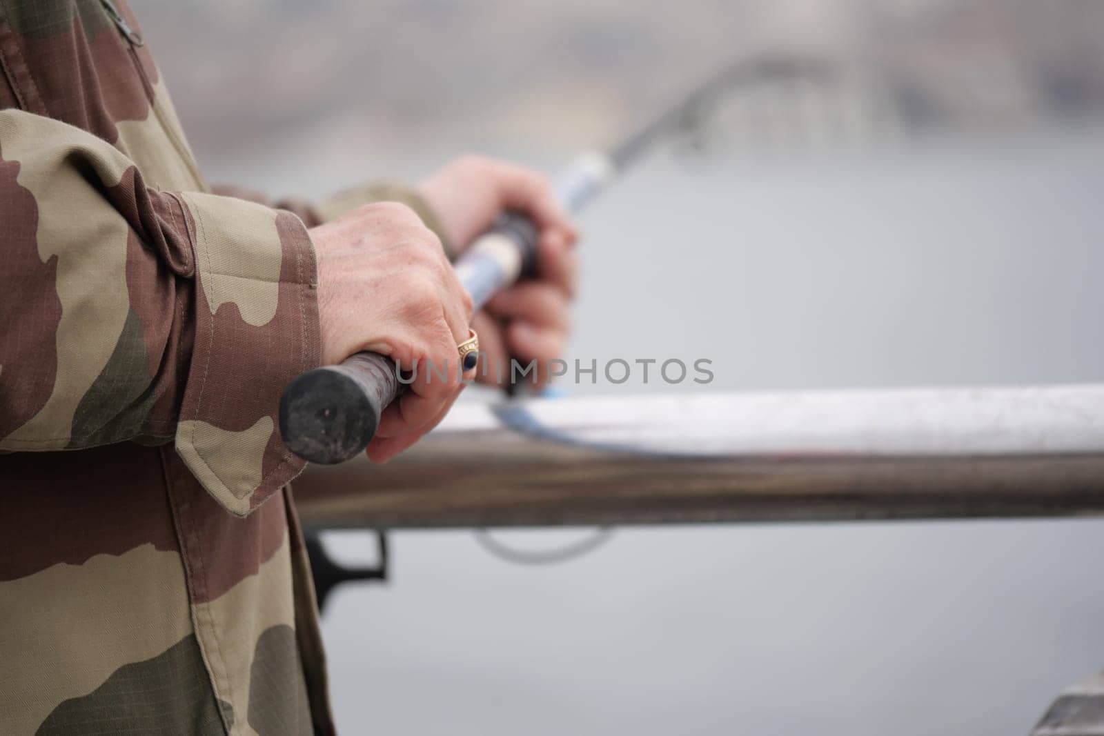 Fisherman grips fishing rod while standing on a pier.