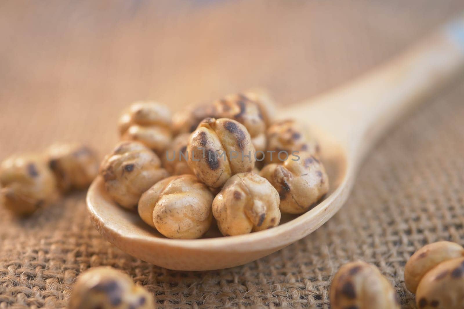Crunchy roasted chickpeas rest in a wooden spoon on burlap fabric.