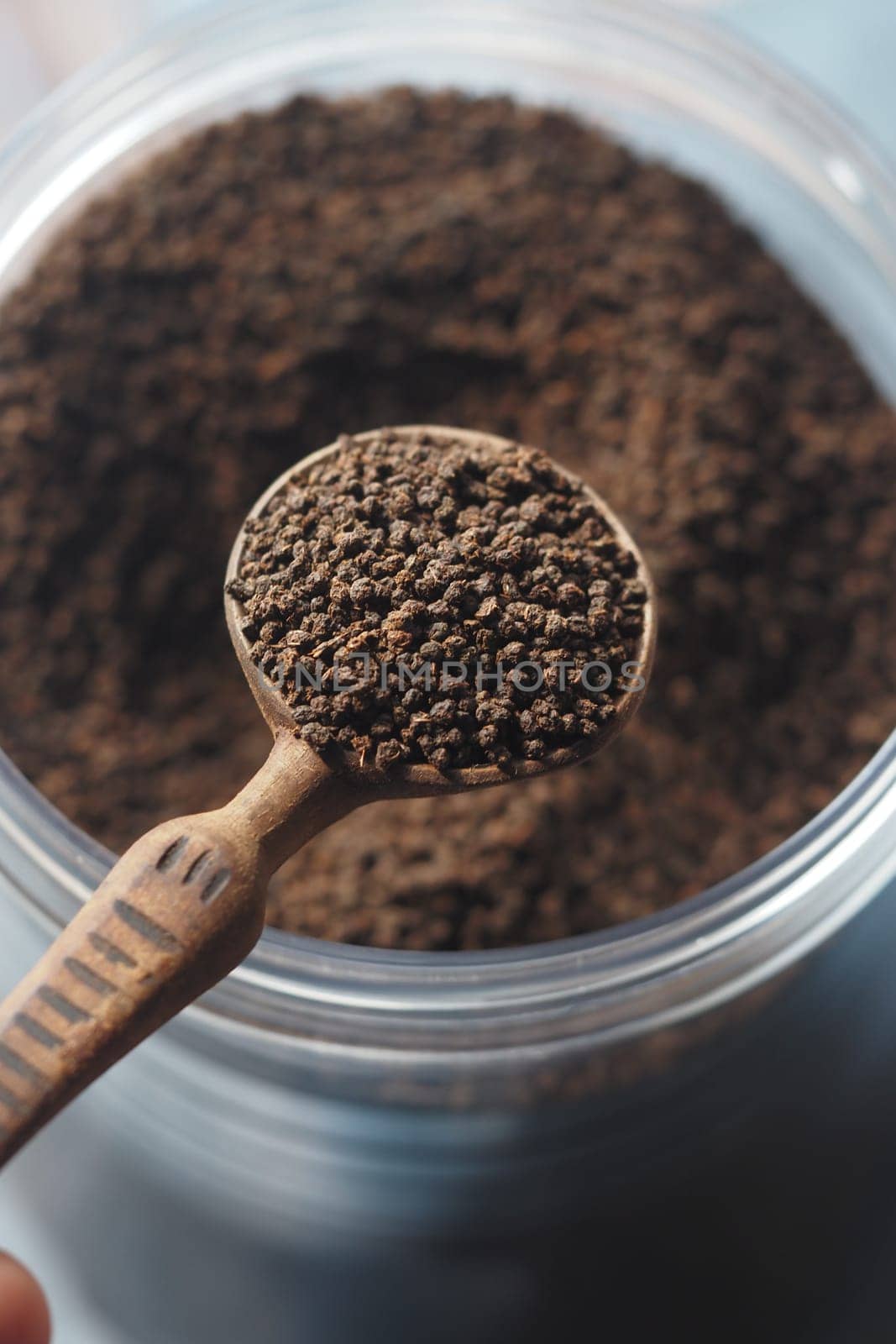loose tea in a wooden scoop over a jar of coffee grounds.