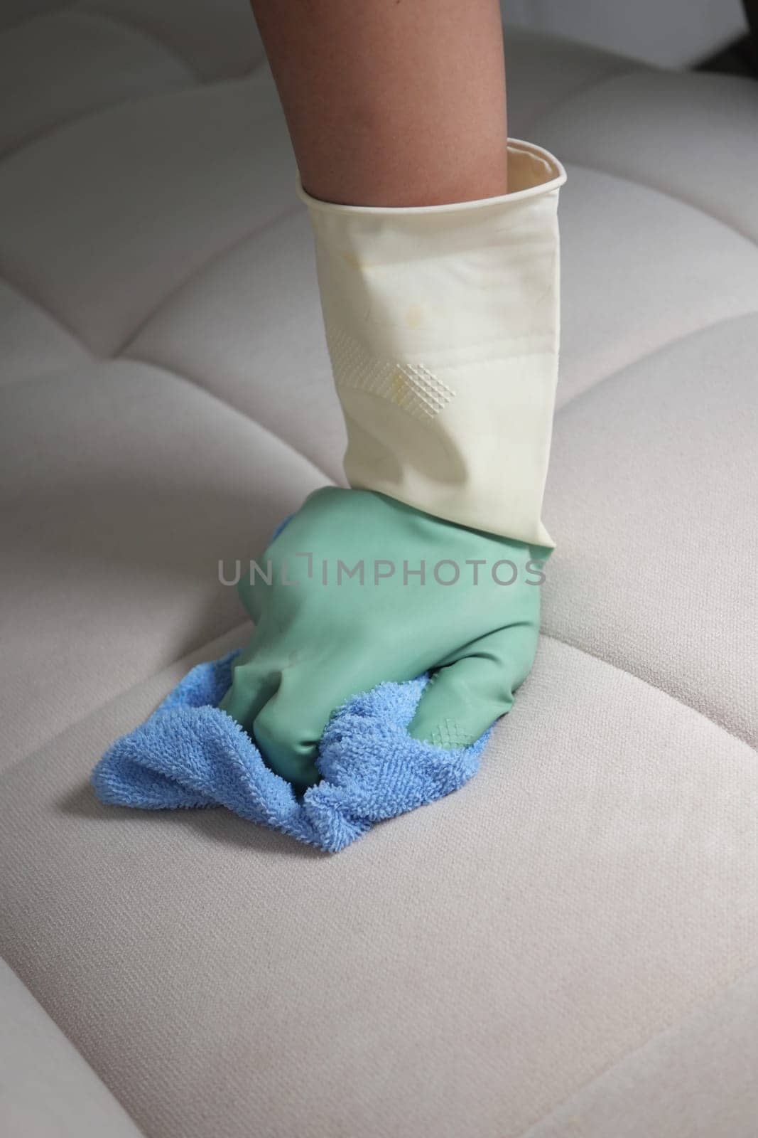 A hand wearing a glove wipes a sofa cushion with a cloth during cleaning.