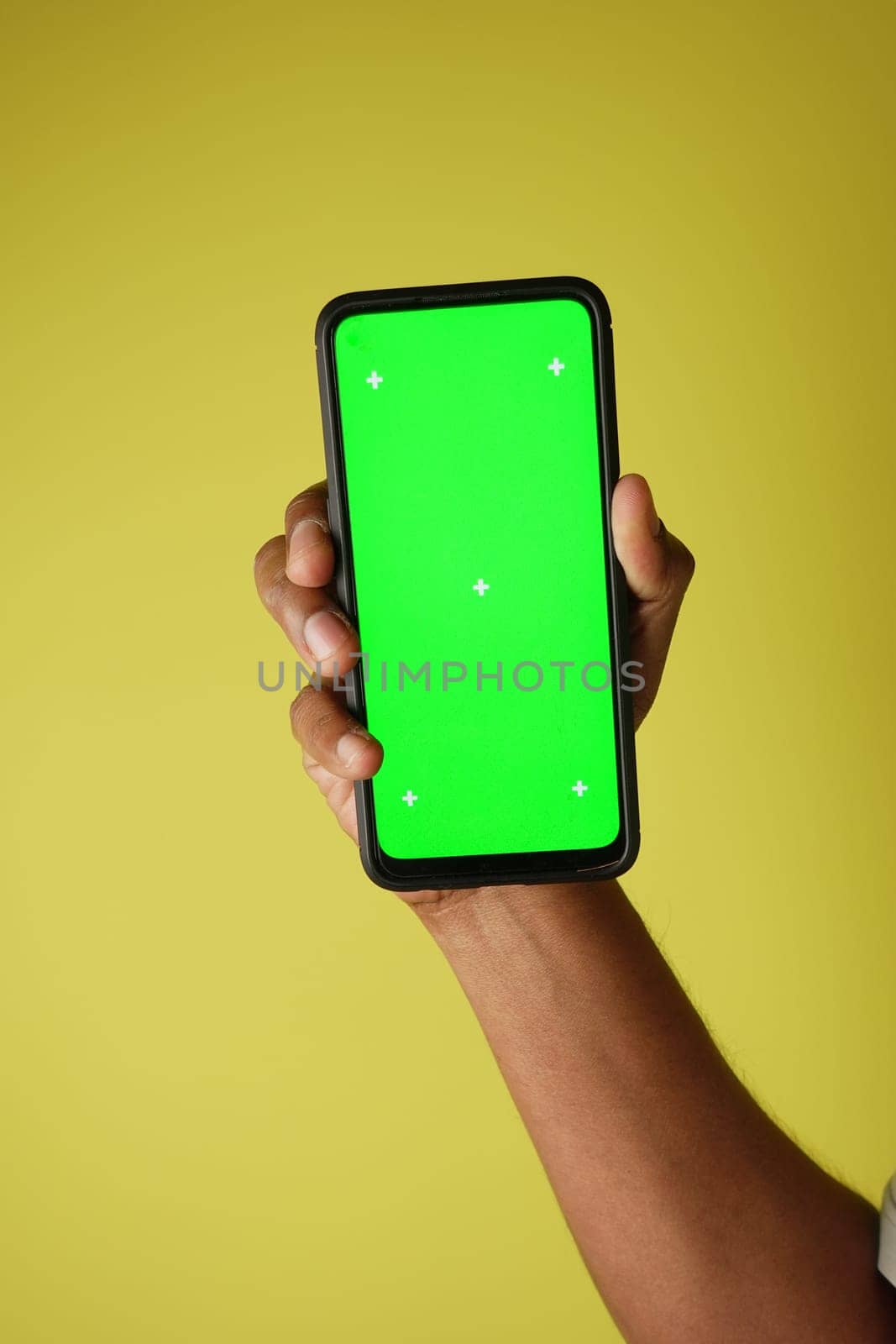 A person holds a smartphone displaying a bright green screen against yellow.