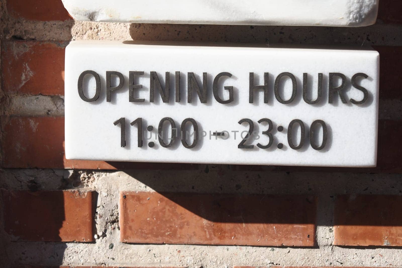 Sign showing opening hours from 11 AM to 11 PM in a brick setting.