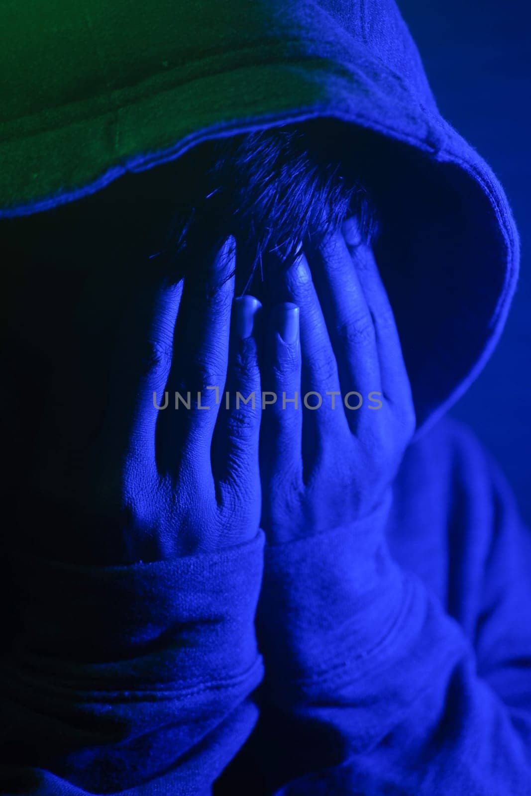 A person covers their face in distress under blue lighting at night.