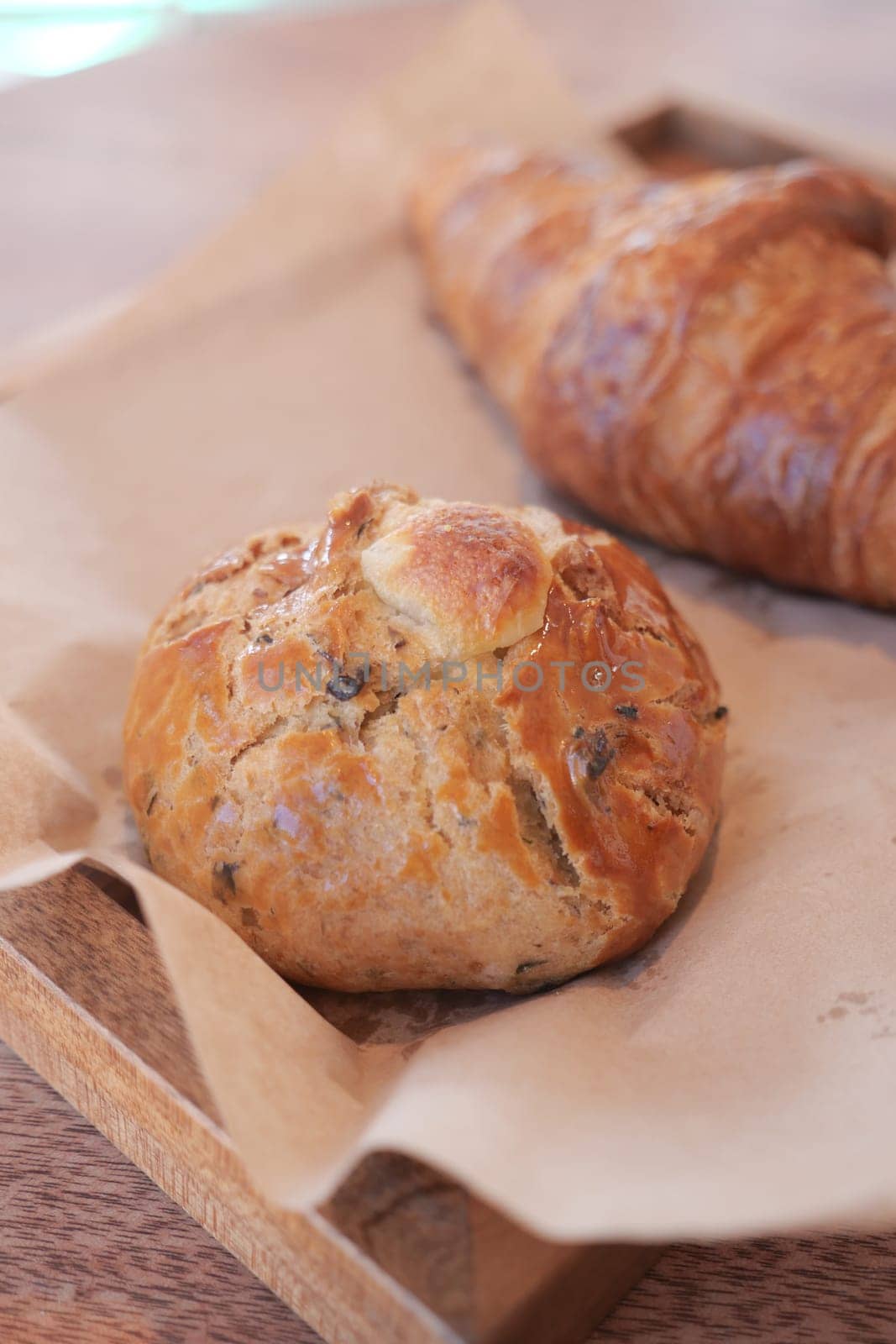 A rustic wooden tray holds freshly baked bread rolls and croissants.