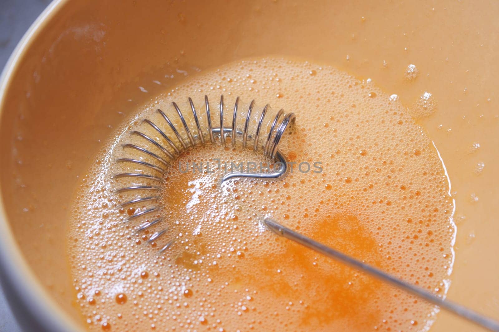 A silver whisk blends egg mixture with bubbles in a light bowl.