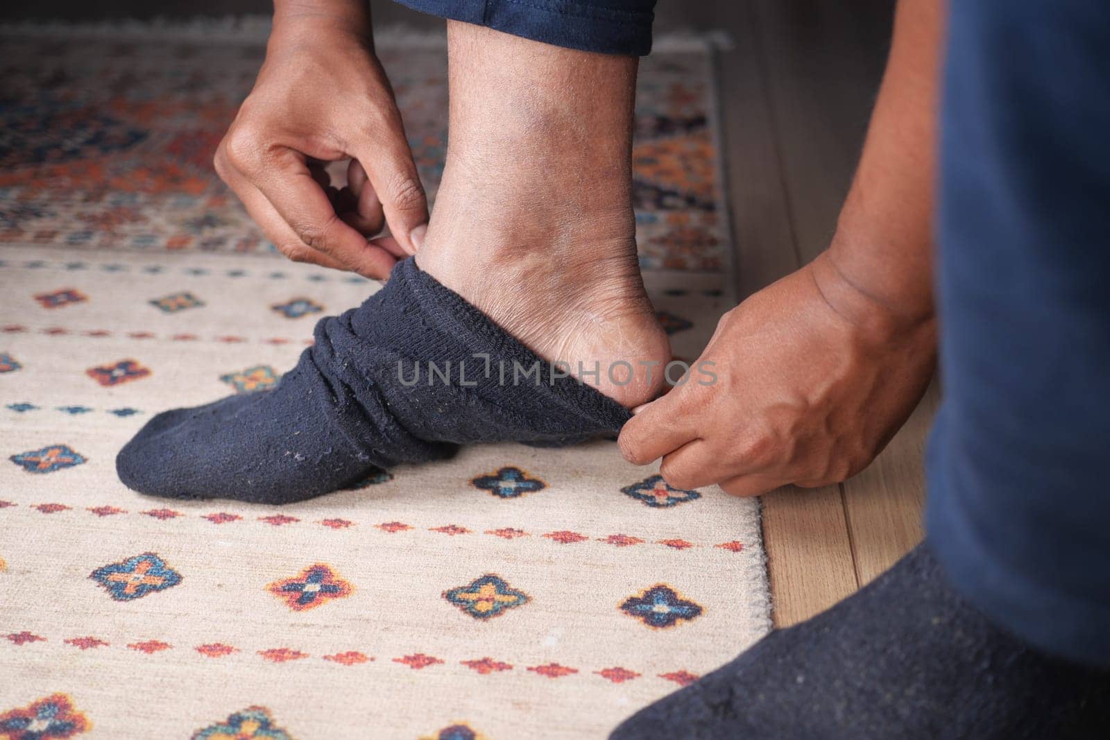 Someone is pulling on a sock while sitting on a rug indoors.