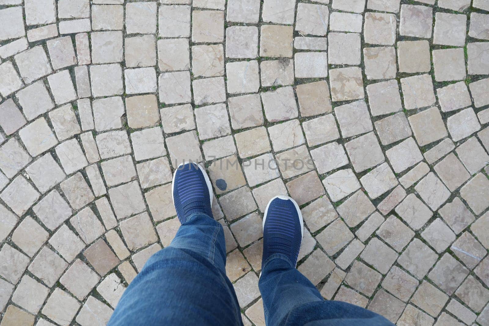 Casual shoes on a circular cobblestone pattern during a daytime walk.