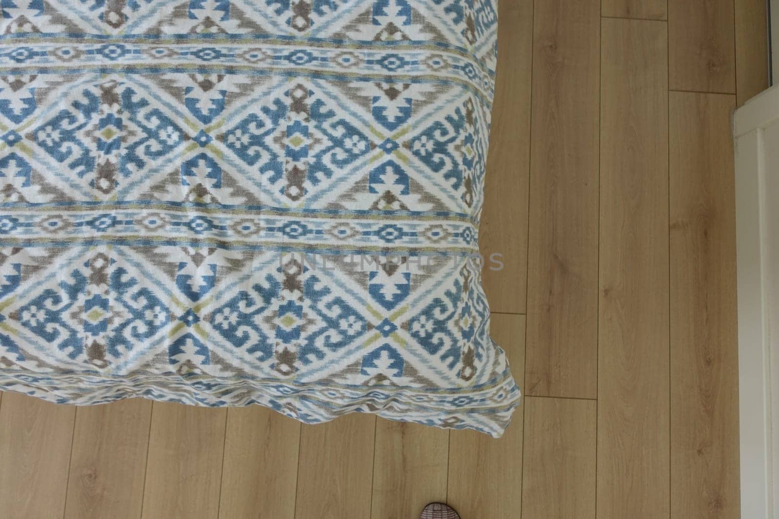 A cozy blanket with an intricate design rests on a light wooden floor.