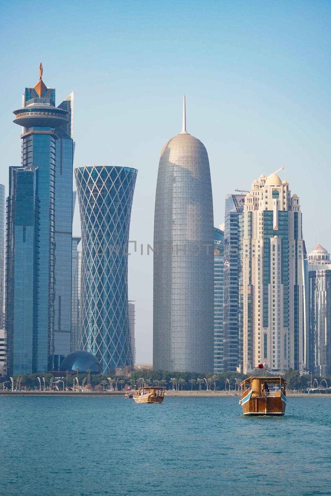 Traditional wooden boats float in the water by a modern city skyline.