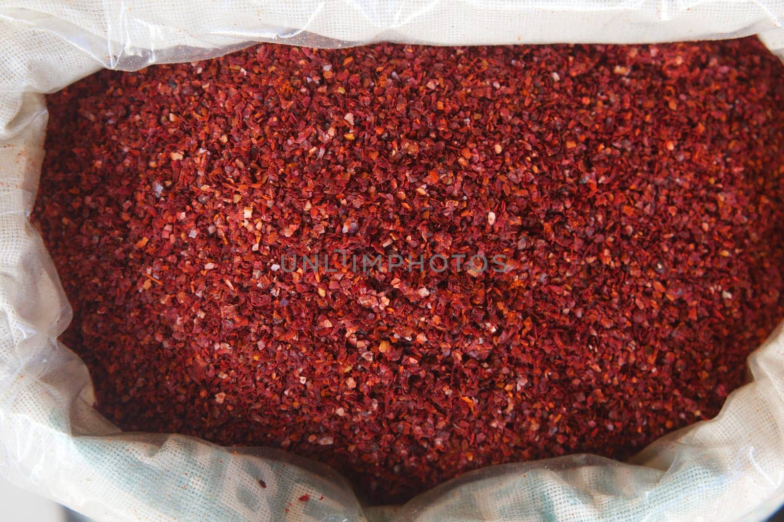 Bright red spices fill a burlap sack at a bustling market stand.