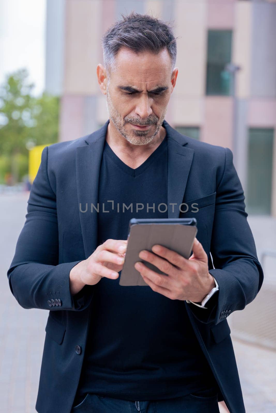 Confident businessman standing outdoors using a tablet in a modern urban setting.He appears focused and professional. Concept of digital work, technology, and contemporary business lifestyle. Vertical