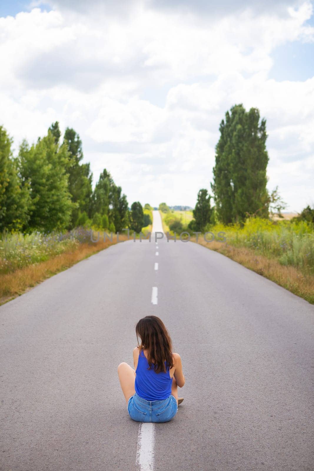 Attractive girl sitting on the asphalt and posing in the middle of the asphalt road near the field, copy space for content.